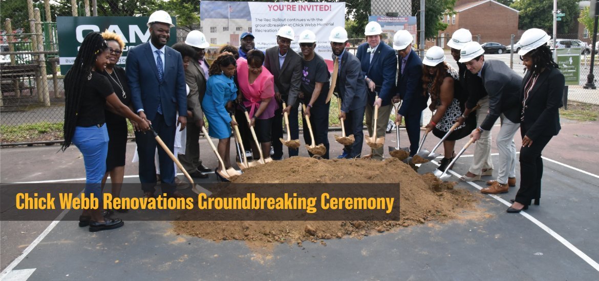 People gathered around a dirt pile, shoveling dirt to represent the breaking of ground of the Chick Webb facility